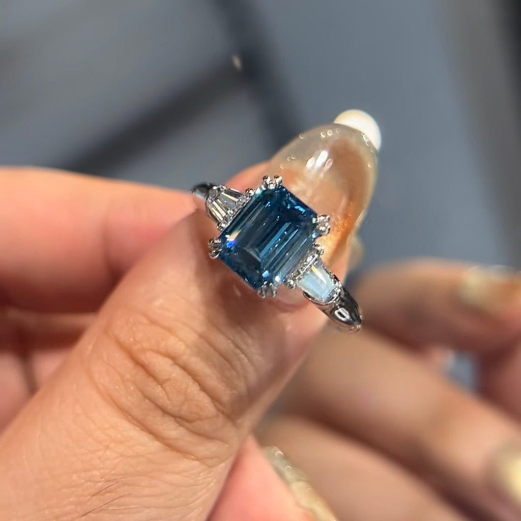 Blue fancy vivid diamond ring held between fingers against a neutral background