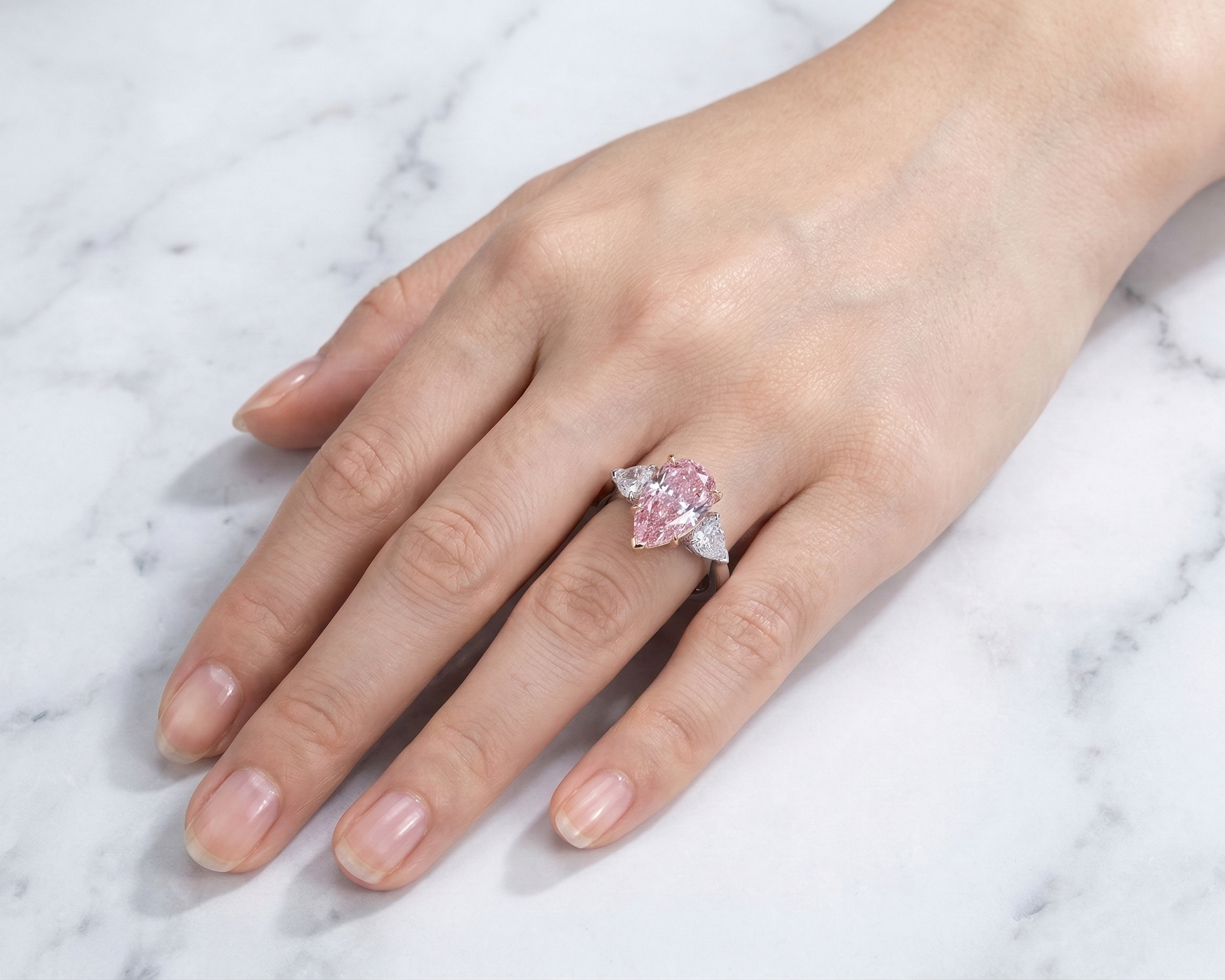 a trilogy diamond ring with fancy vivid pink diamond pear cut and white side diamonds on a platinum band 