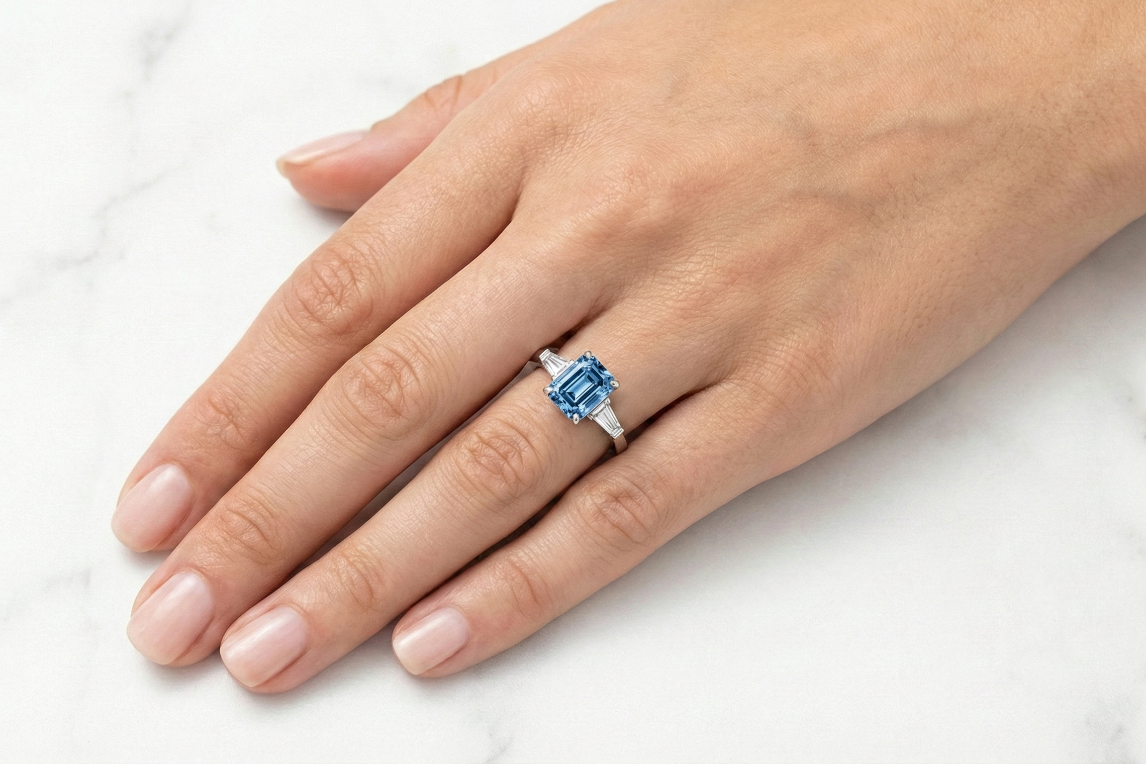 Hand wearing a ring with a diamond trilogy platinum ring on a white background