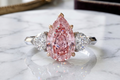 a trilogy diamond ring with fancy vivid pink diamond pear cut and white side diamonds on a platinum band 