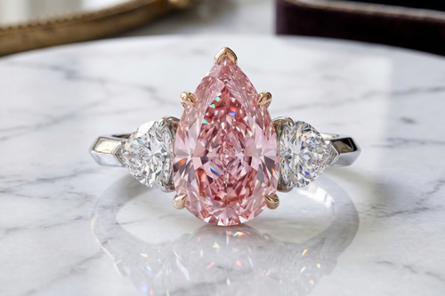 a trilogy diamond ring with fancy vivid pink diamond pear cut and white side diamonds on a platinum band 