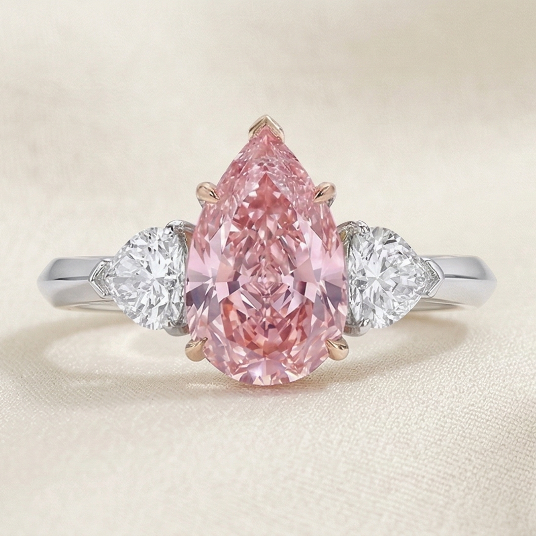 a trilogy diamond ring with fancy vivid pink diamond pear cut and white side diamonds on a platinum band 