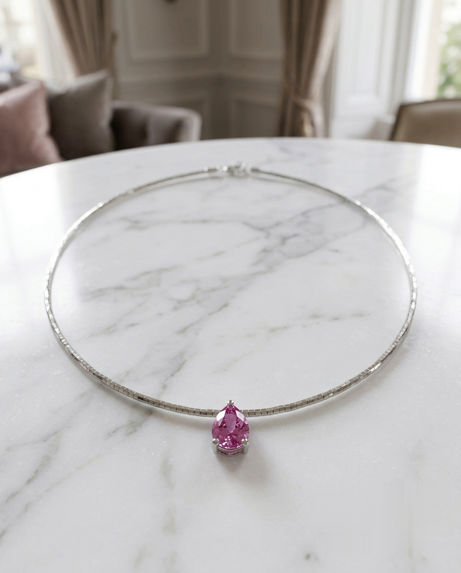 The Rosewater Drop pink sapphire necklace — pear-cut padparadscha-pink sapphire pendant on a fine silver collar, on a marble table