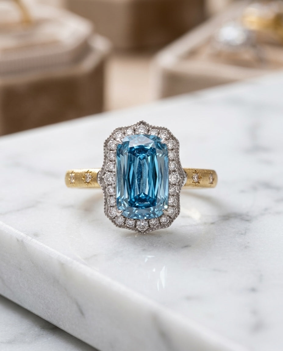The Tidal Vow — lab-grown blue diamond ring in 18K gold with a scalloped white diamond halo, on marble